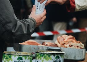 Hands exchanging a drink outdoors, surrounded by juice cartons and bread, evoking a communal sharing atmosphere.